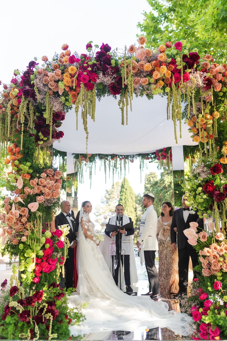 Todd Bronshtein officiating a Jewish wedding ceremony beneath a chuppah covered in flowers
