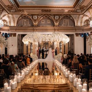 A candlelit wedding ceremony beneath a floral chuppah in a grand ballroom
