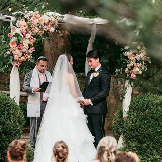 A bride and groom exchange vows beneath a flower-trimmed chuppah, a ceremony that brought two family traditions together