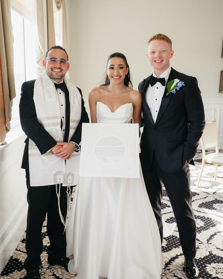 Todd Bronshtein smiling with a bride and groom who are holding their ketubah